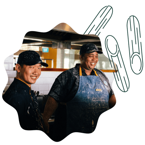 Two chefs in a professional kitchen smiling while preparing food together.